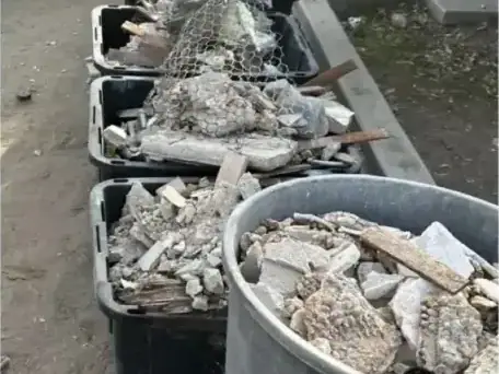 Broken concrete in bins and a trash can beside a lawn