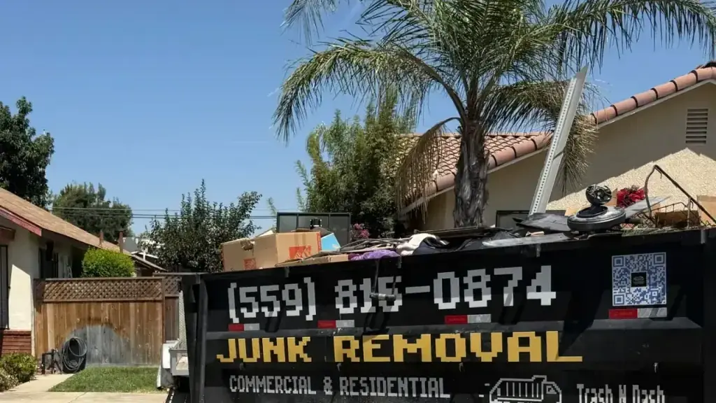 The black Trash N Dash dump trailer loaded to the top in front of a house with a palm tree