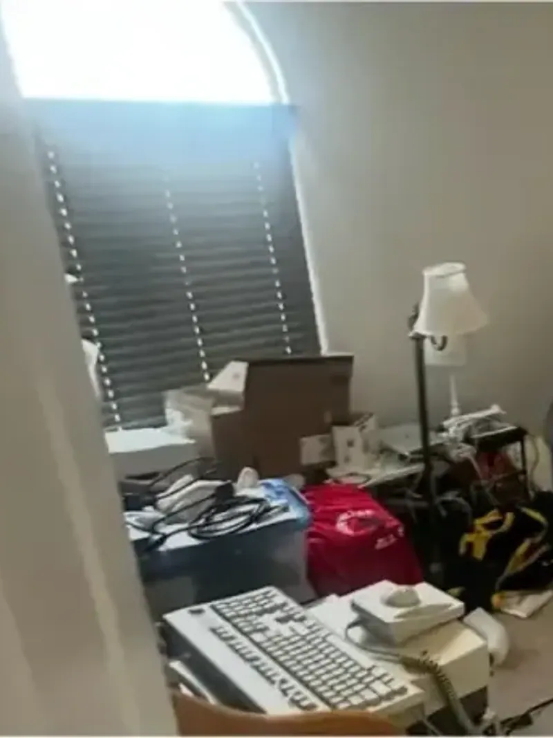 A cluttered room with a desk a chair and boxes on the floor