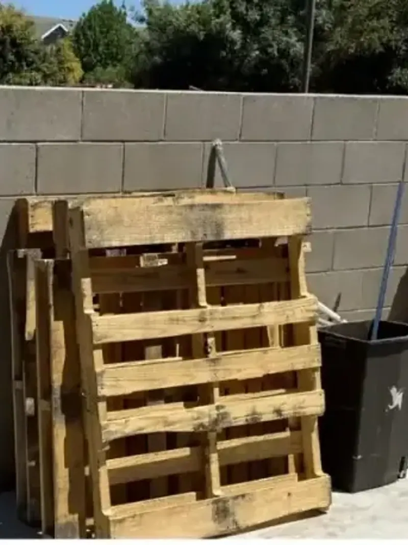 Pallets and old appliances stacked against a block wall at a commercial lot