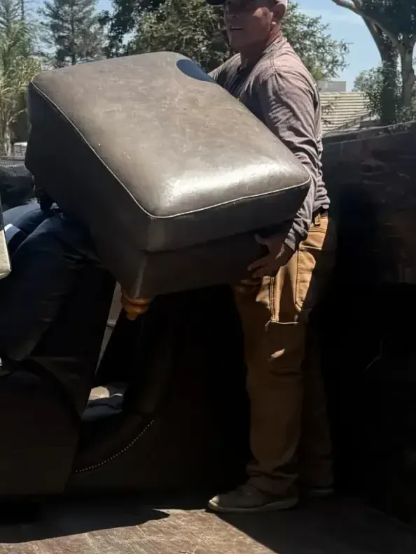 A crew member lifting a grey sofa section into the trailer