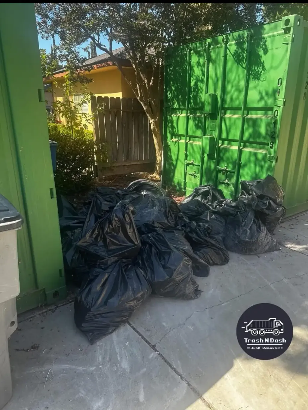 Bagged waste piled beside shipping containers before pickup