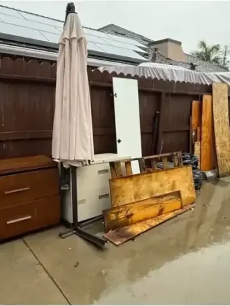 A wet patio with an old dresser cabinets and an umbrella against a fence